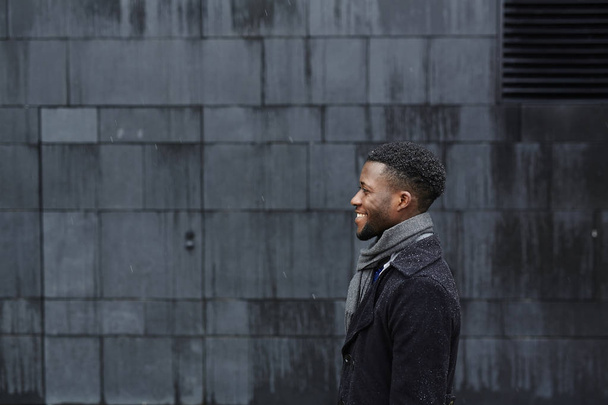 Boční pohled na usmívající se muž v černém kabátě a šedá šála - Fotografie, Obrázek