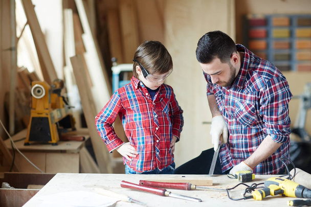 Petit garçon et son père sculptant le bois en atelier
 - Photo, image