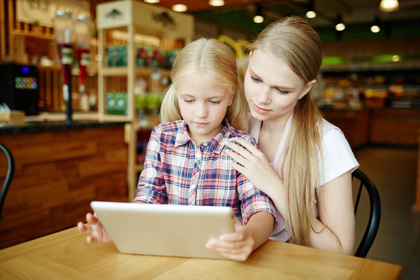 Mujer joven y su hija eligiendo la comida del menú en línea en la cafetería moderna en el ocio
 - Foto, Imagen