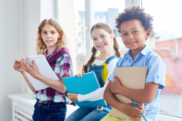 Gruppe von Kindern mit Kopierbüchern und Bleistiften sitzt am Klassenzimmerfenster - Foto, Bild
