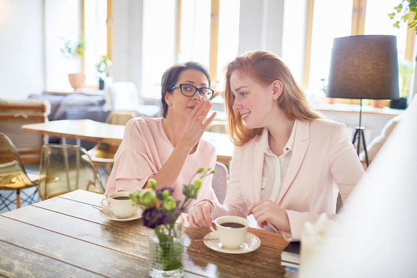 Милый менеджер средних лет в очках делится сплетнями с коллегой, пока они проводят кофе-брейк в прекрасном ресторане с панорамными окнами
 - Фото, изображение