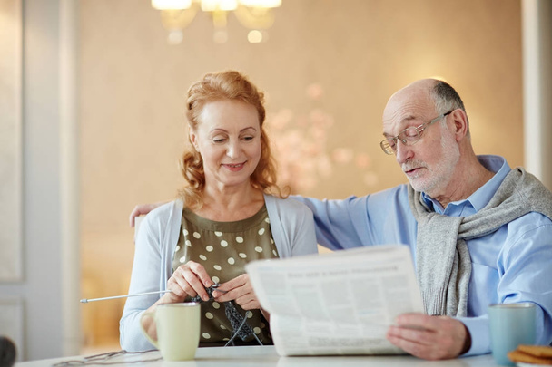 Mature woman knitting while her husband reading her newspaper - Photo, Image