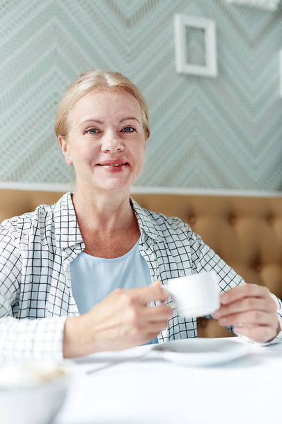 Happy senior blonde with cup of tea or coffee relaxing in cafe - 写真・画像