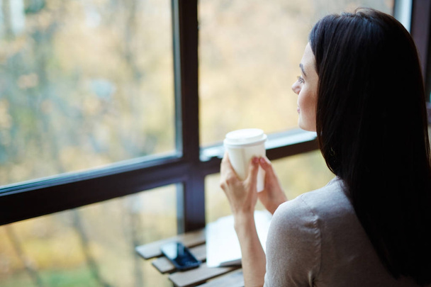 Adolescente hembra con bebida mirando por la ventana
 - Foto, imagen