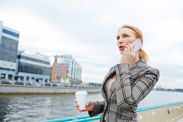 Elegant businesswoman with drink speaking by smartphone during trip by steamship - Fotoğraf, Görsel