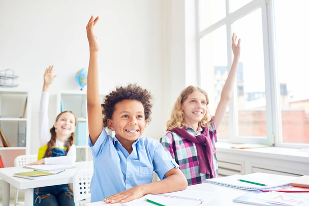 Ευτυχισμένη και έξυπνο μαθητές του δημοτικού σχολείου, αυξάνοντας τα χέρια τους στο μάθημα - Φωτογραφία, εικόνα