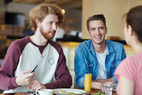Onnelliset kaverit puhuvat bändikaverinsa kanssa lounaaseen mennessä luokkien välillä college kahvilassa
 - Valokuva, kuva