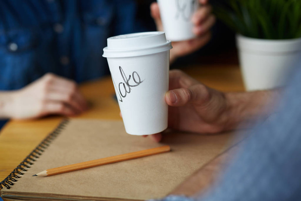 Closeup shot of two paper coffee cups with names on them in hands of young people working in cafe - Photo, Image