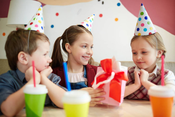 Adorable girl looking at birthday surprise being given by her friend - Foto, imagen