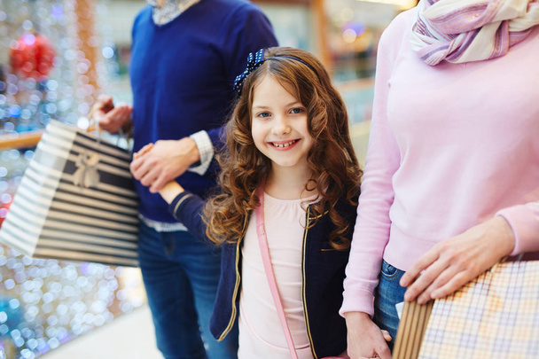 Jolie petite fille avec des cheveux bouclés faisant du shopping avec les parents
 - Photo, image