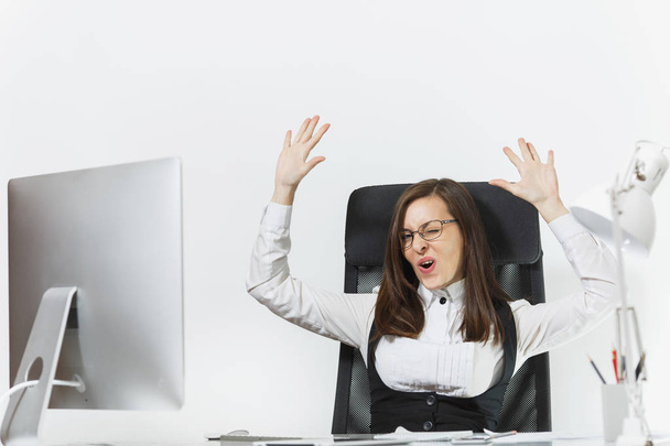 Smiling business woman sitting at the desk, working at computer with modern monitor and documents in office, rejoicing at success, holding hands up on white background, copy space for advertisement - Photo, Image