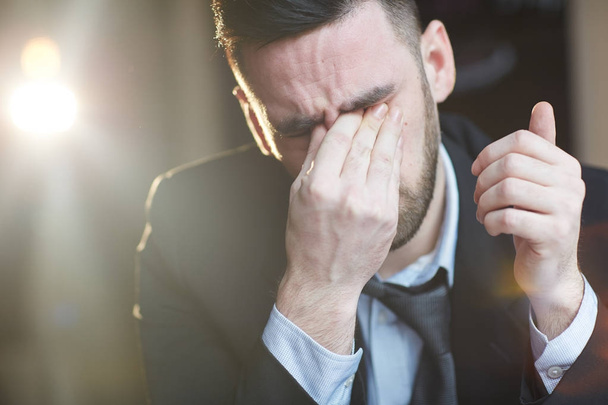Портрет втомленого дорослого чоловіка, що розтирає очі і плаче на чорному тлі з спалахом лінзи
 - Фото, зображення