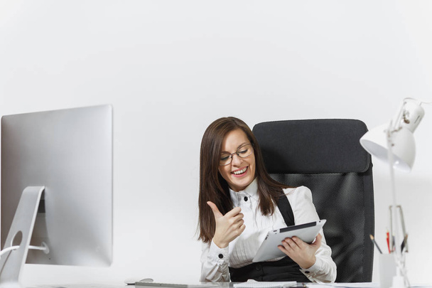 Dość uśmiechający się biznes brązowy włosy kobieta w garnitur i okulary, siedząc przy biurku, Wyświetlono kciuk w, praca przy komputerze z nowoczesnego monitora z dokumentu i tablet w biurze światła na białym tle - Zdjęcie, obraz