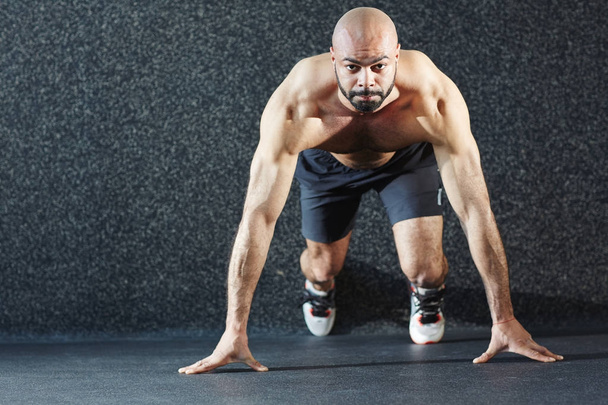 Retrato motivacional do homem musculoso sem camisa em pé na posição inicial determinado a correr longa distância, olhando para a câmera
 - Foto, Imagem