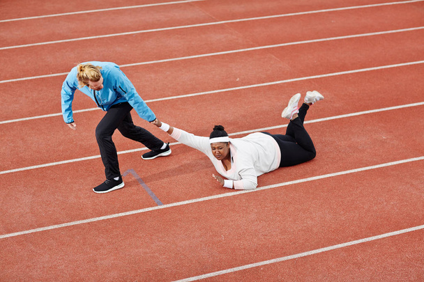 Kalıcı eğitmen isteksiz artı-size kadın bitiş çizgisine doğru yarış pisti boyunca çekerek - Fotoğraf, Görsel