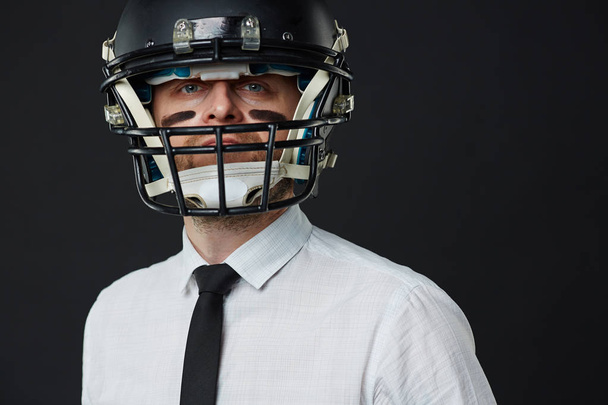 Closeup portrait of middle aged man wearing white shirt, tie and American football helmet with army paint on his face looking at camera - Photo, Image