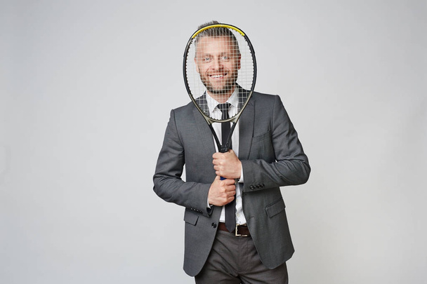 Sorridente uomo d'affari di mezza età che guarda la fotocamera attraverso la racchetta da tennis sullo sfondo grigio
 - Foto, immagini