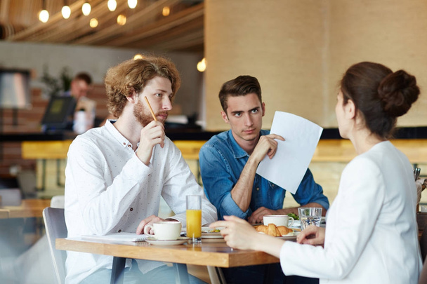 Unrecognizable young designer sharing ideas concerning start-up project with her handsome colleagues while having working meeting at modern cafe, blurred background - Photo, Image