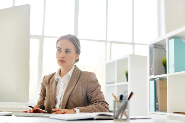 mulher sentada na frente do computador e analisando os resultados do trabalho realizado, janelas panorâmicas do escritório moderno em segundo plano
 - Foto, Imagem