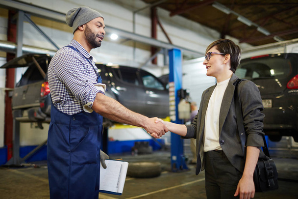 Car repairman and his client handshaking in garage - Photo, Image