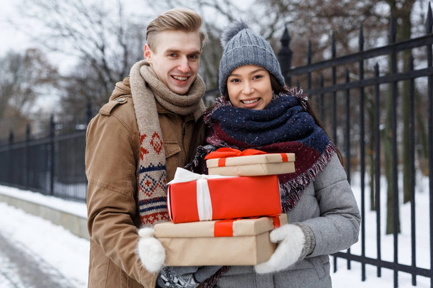 junges Paar mit Weihnachtsgeschenken spaziert an winterlichem Tag - Foto, Bild