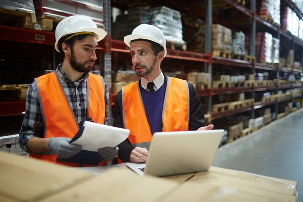 Портрет двух работников склада, делающих инвентаризацию склада, менеджер разговаривает с погрузчиком при использовании ноутбука для ввода данных из списка товаров
 - Фото, изображение