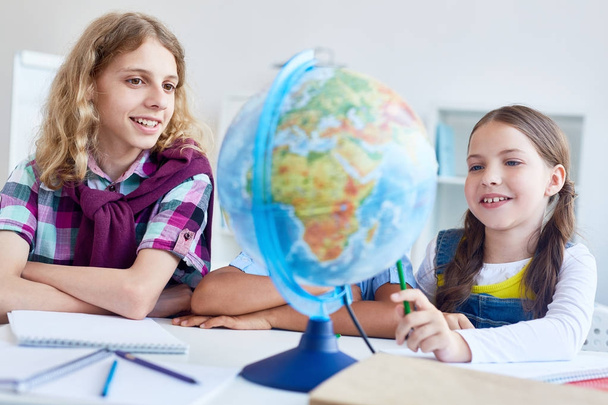 Twee klasgenoten kijken naar globe model en landerijen te bespreken - Foto, afbeelding