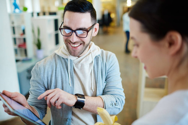 Portrait of modern man pointing at tablet and smiling while discussing work with his colleague in open office space - Foto, Bild