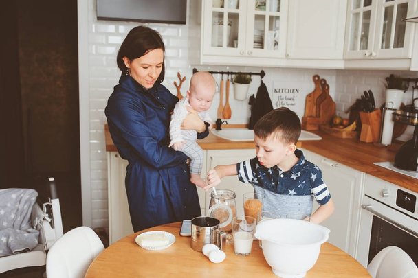 famille heureuse cuisiner ensemble dans la cuisine blanche moderne. Mère, fils et fille cuisinant dans le week-end confortable matin à la maison
 - Photo, image
