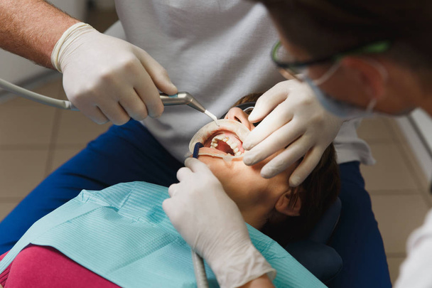 Lähikuva valmisteluun ja asentamiseen hampaiden keraaminen kruunu. Mies ammatillinen hammaslääkäri auttaa hoitamaan hampaita naisen potilaan klinikalla kevyt toimisto moderneilla työkaluilla laitteet. Suu auki
. - Valokuva, kuva