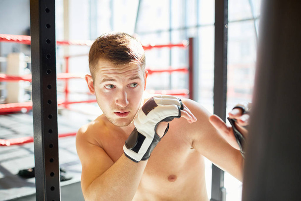 Deportista sin camisa pateando saco de boxeo en el gimnasio
 - Foto, imagen
