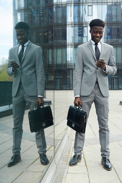 Busy entrepreneur with smartphone and briefcase messaging outdoors - Photo, Image