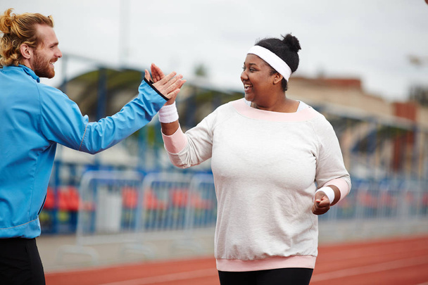 Happy plus-size woman giving high five to her personal trainer while running on track - Fotó, kép