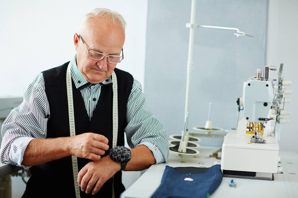 Portrait of old man working in tailoring studio making clothes at sewing machine - Foto, Bild