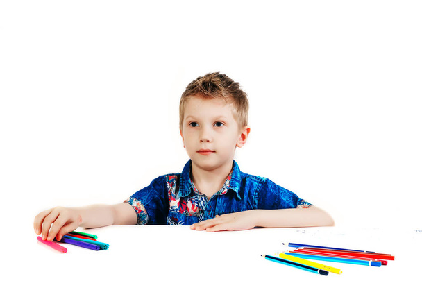 Ein 6-jähriger Junge im blauen Hemd malt mit Bleistiften auf weißem Hintergrund. - Foto, Bild