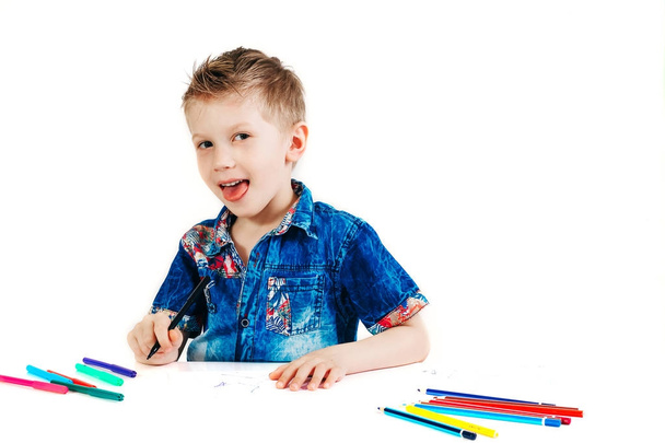 A 6 year old boy in a blue shirt paints with pencils on a white background isolate - Foto, Bild