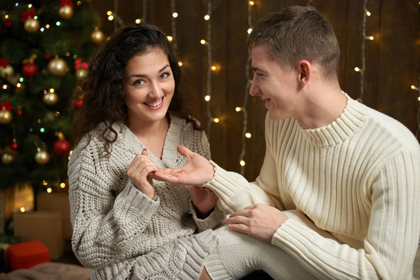 muž dává dívka zásnubní prsten, pár v vánoční osvětlení a dekorace, oblečeni v bílém, jedle na tmavém pozadí dřevěná, Zimní dovolená concept - Fotografie, Obrázek