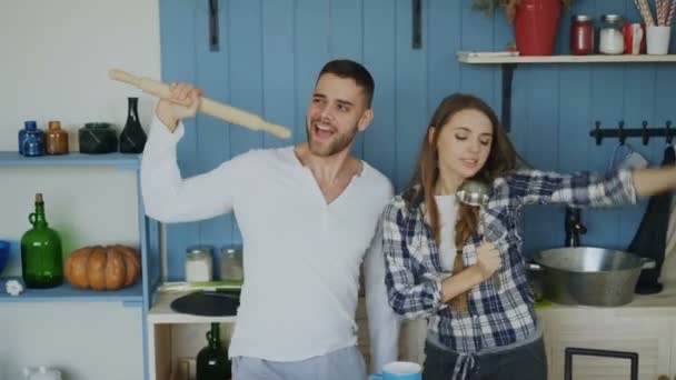 Young joyful couple have fun dancing and singing while set the table for breakfast in the kitchen at home - Πλάνα, βίντεο