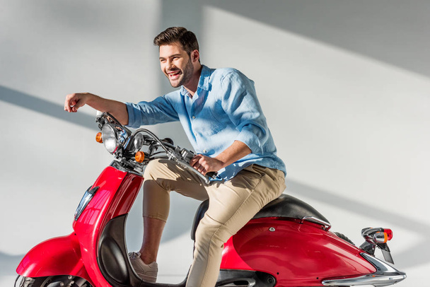 side view of young cheerful man sitting on red scooter - Fotoğraf, Görsel