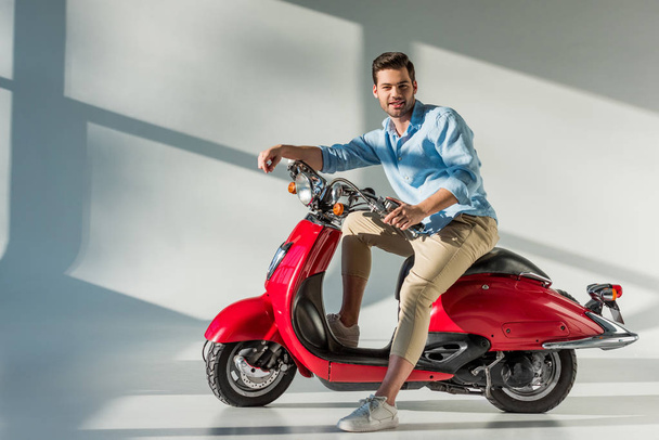 side view of young man looking at camera while sitting on red scooter - Photo, Image