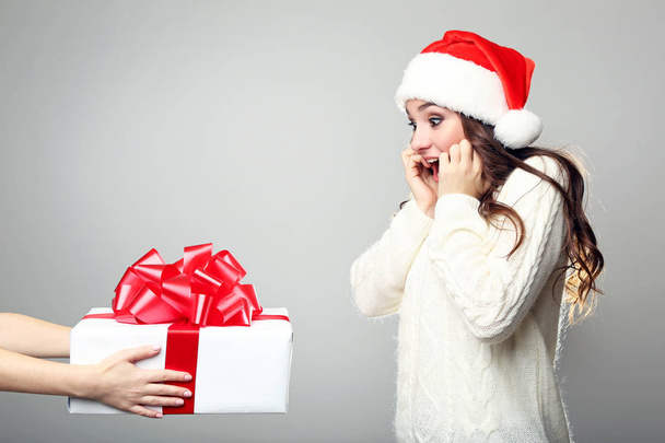 Young woman in santa hat gets a gift box on grey background - Фото, зображення