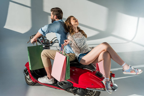 stylish couple in love with shopping bags sitting on red scooter - Photo, Image