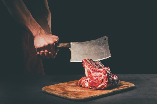 carnicero cortar carne cruda con cuchilla en tabla de cortar de madera
 - Foto, Imagen
