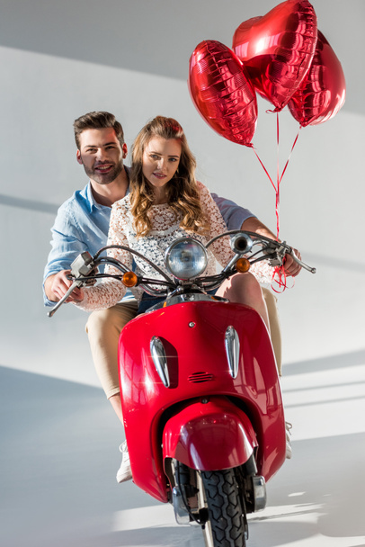 couple with red heart shaped balloons riding red scooter together - Foto, Imagen