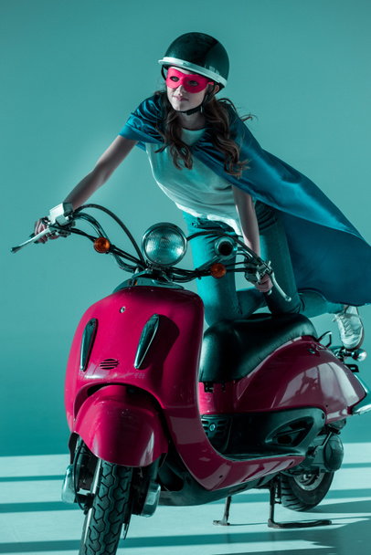 woman in superhero mask and cape and protective helmet on red scooter - Foto, Imagem