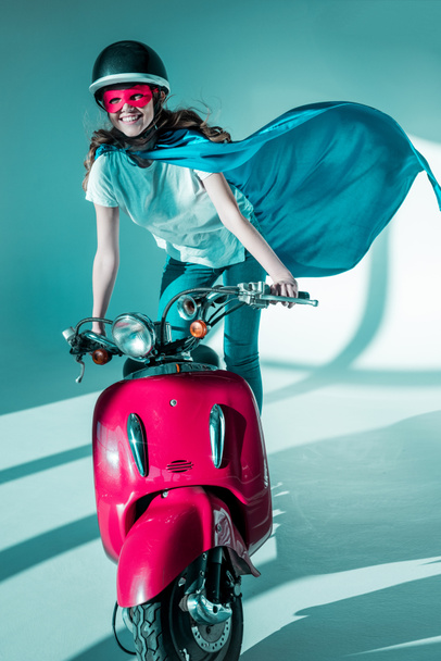 smiling woman in superhero costume and protective helmet on red scooter - Foto, imagen