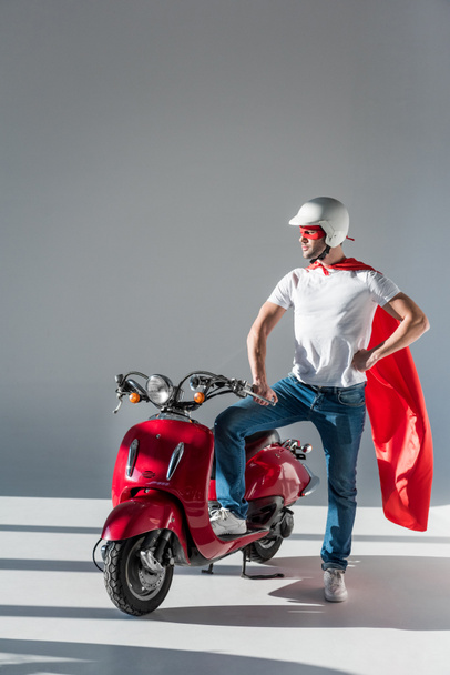 man in protective helmet and superhero costume standing at red scooter - Fotó, kép