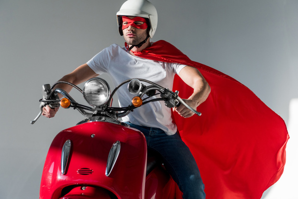 Mann mit Schutzhelm und Superheldenkostüm fährt roten Roller - Foto, Bild
