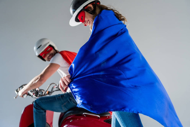 selective focus of couple in helmets and superhero capes on scooter - Foto, imagen
