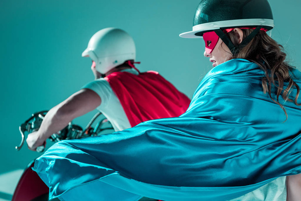 selective focus of couple in helmets and superhero capes on scooter - Photo, Image